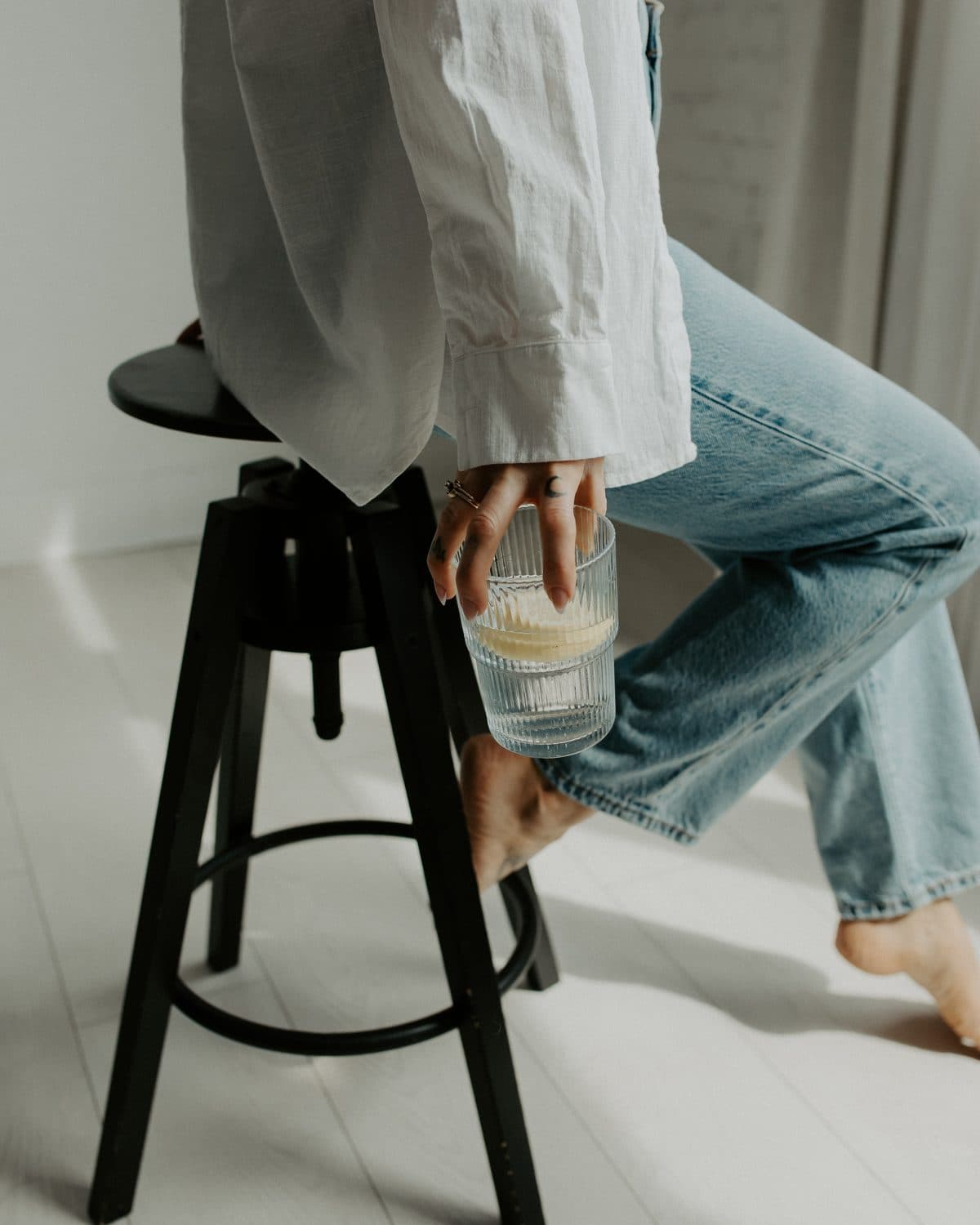 Woman in a white shirt and jeans holding a glass on a black stool